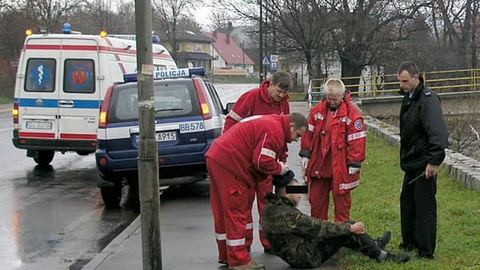 Scenka z ulicy Wolności: ratownicy pogotowia i policjanci próbują podnieść zamroczonego alkoholem człowieka.