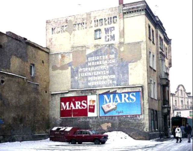 „Reklama” ścienna z lat PRL przez jakiś czas konkurowała z bilbordami, które na poczatku lat 90-tych były w Jeleniej Górze nowością. W tym szarym i smętnym zaułku „wyrosły” delikat