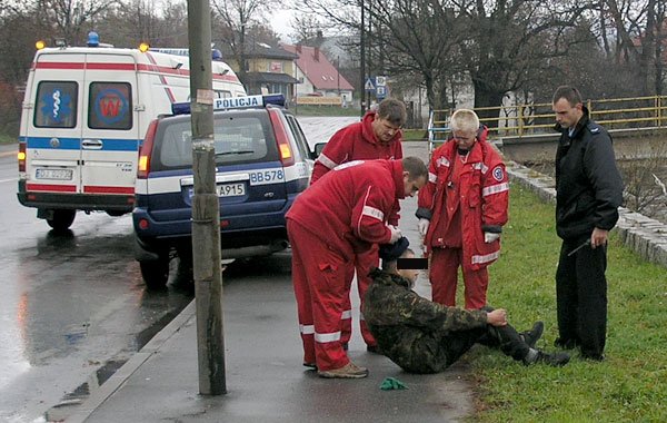 Scenka z ulicy Wolności: ratownicy pogotowia i policjanci próbują podnieść zamroczonego alkoholem człowieka.